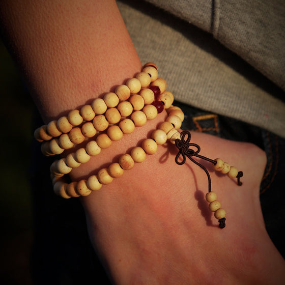 Ett armband Mala. Armbandet är snurrat flera varv runt en handled. Armbandet är gjort av sandelträ.